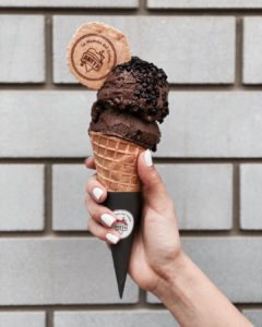 a hand holding a cone with chocolate ice cream and topped with a branded piece of waffle cone