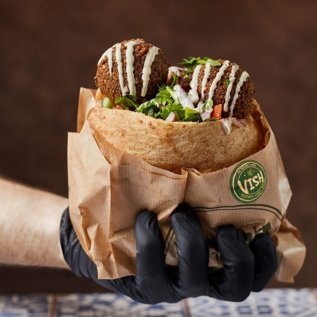 A gloved hand holding a pita full of falafel and salads