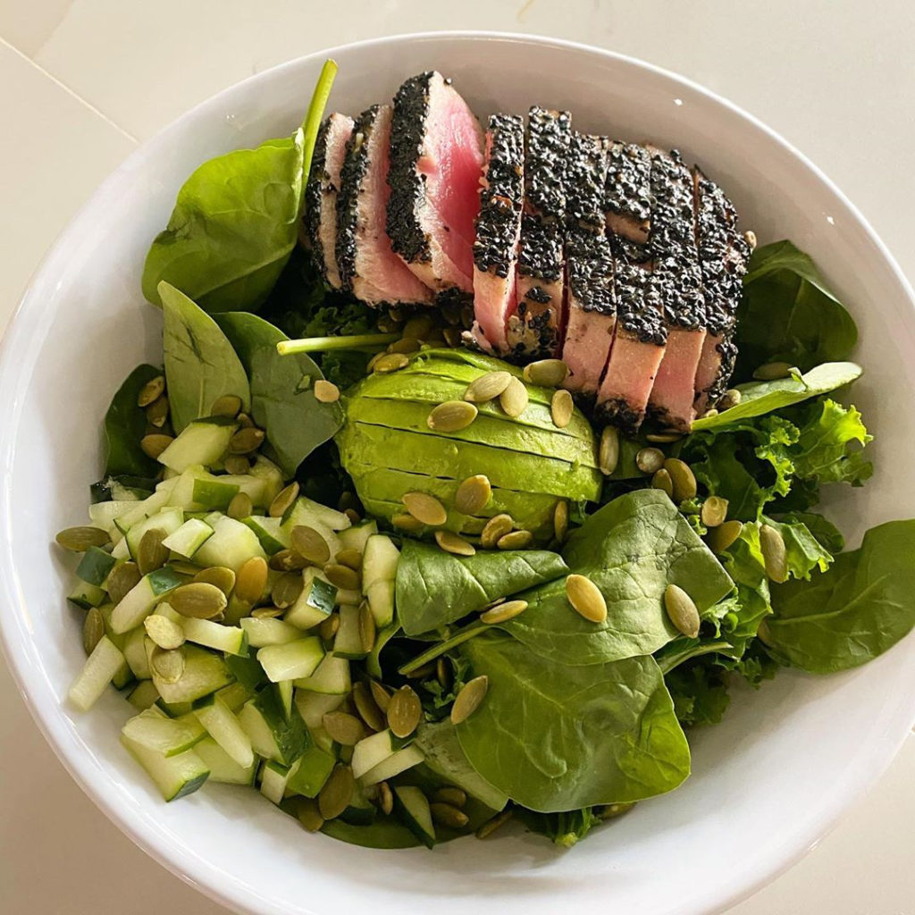 A salad on a bed of greens with apple, pumpkin seeds, avocado and seared tuna
