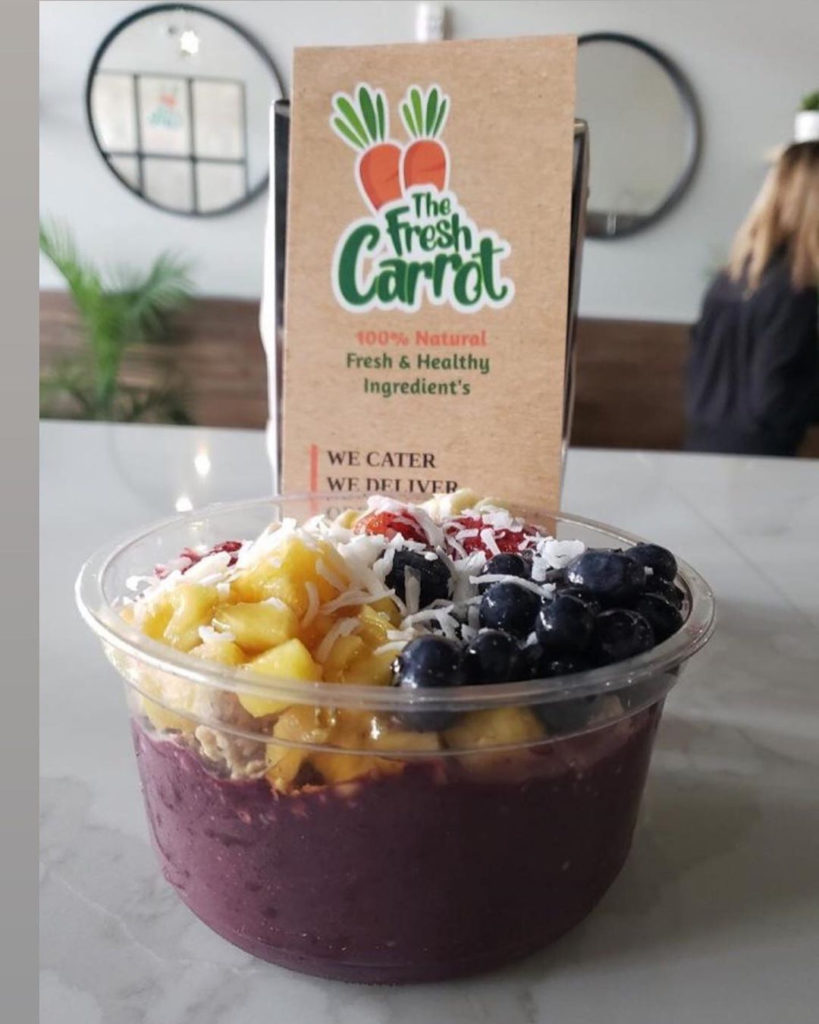 An acai bowl with fresh fruit and coconut in a plastic container
