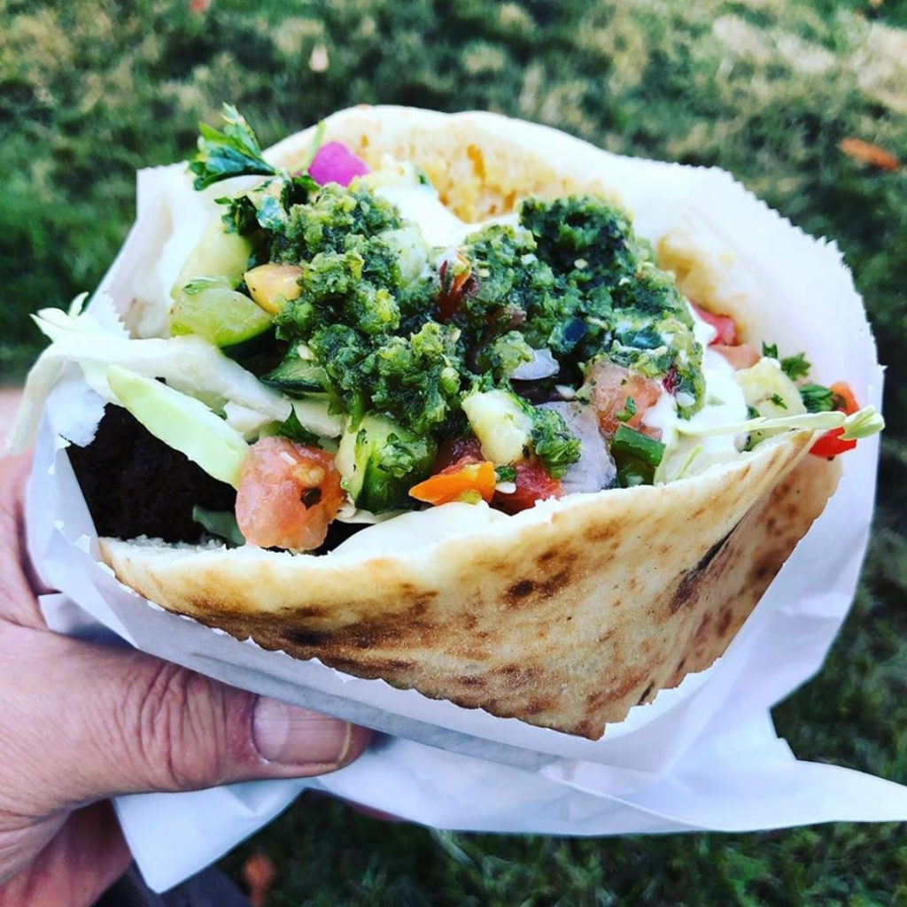 a hand holding a pita filled with falafel and salads