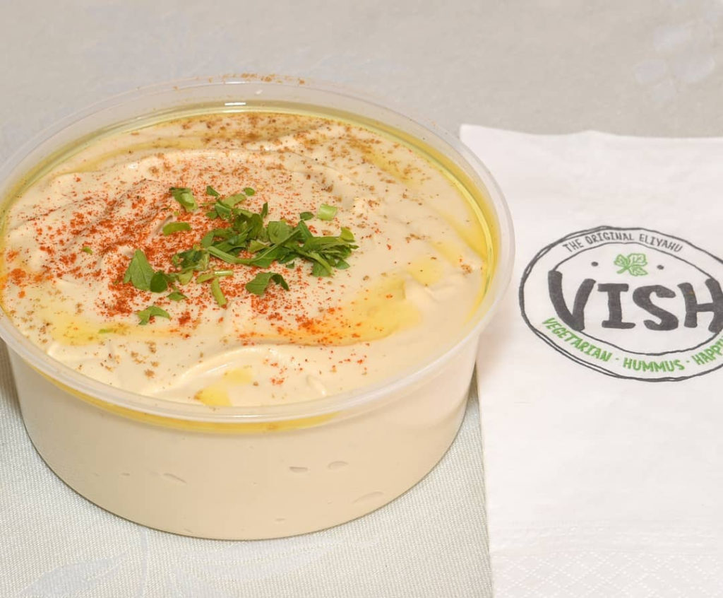 A deli container filled with hummus topped with spices and herbs for takeout
