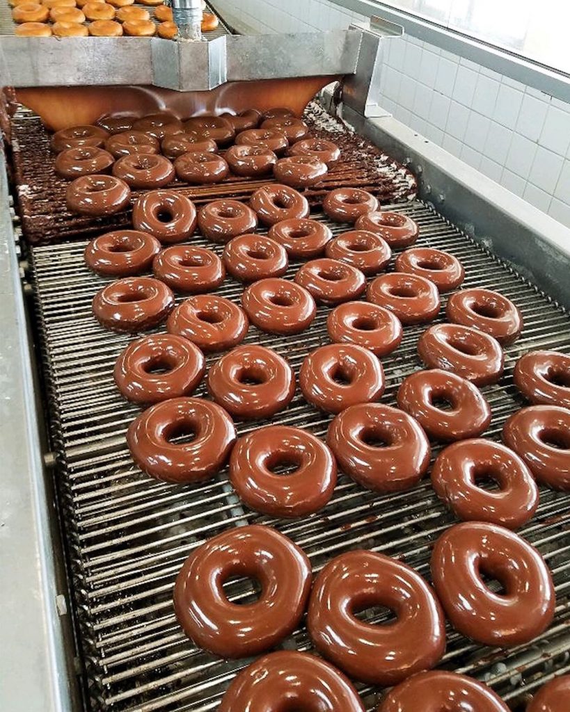 donuts being glazed and moving down a conveyor belt