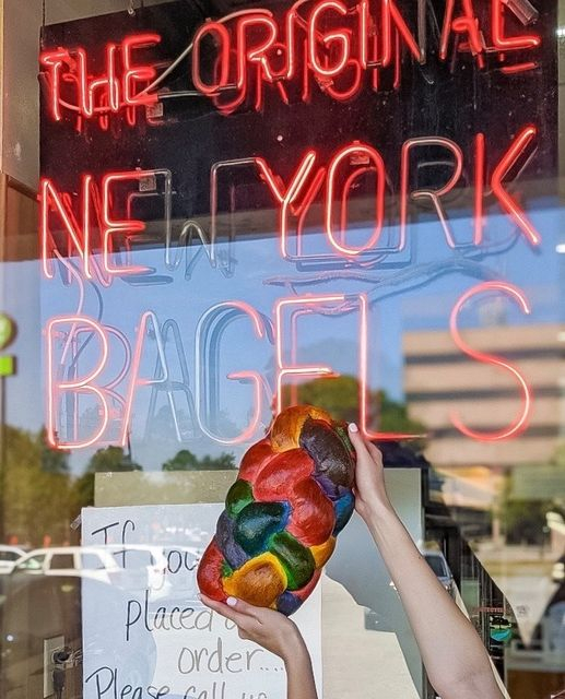 holding a rainbow challah in front of a bagel shop