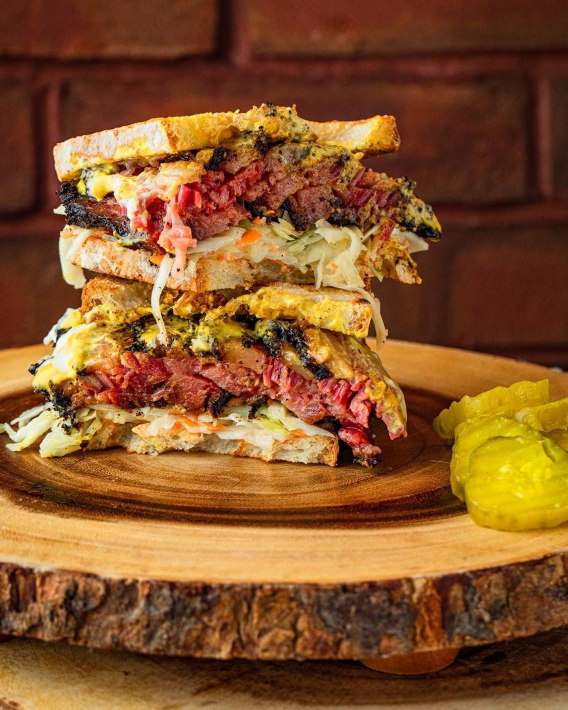 two halves of a stuffed pastrami sandwich stacked on top of each other