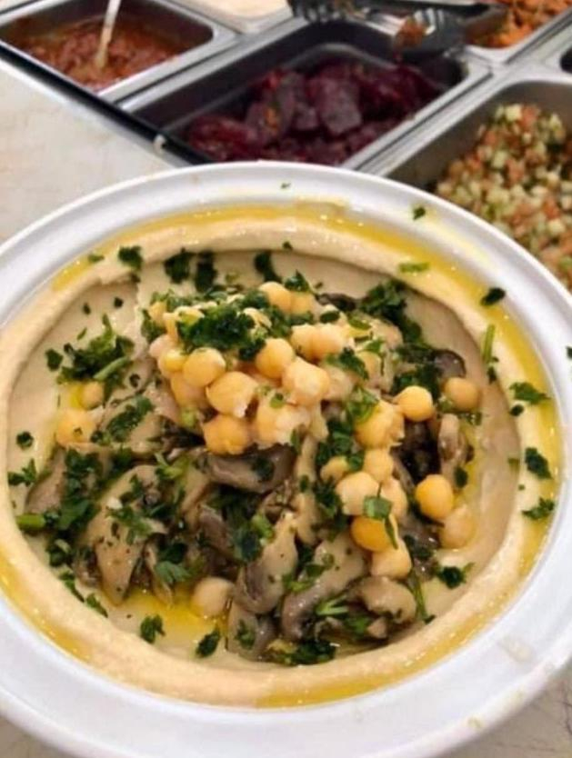 a white hummus bowl with a chickpeas and mushrooms in front of a salad bar