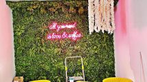 a green grassy wall with pink writing, and yellow chairs and a white table in the foreground