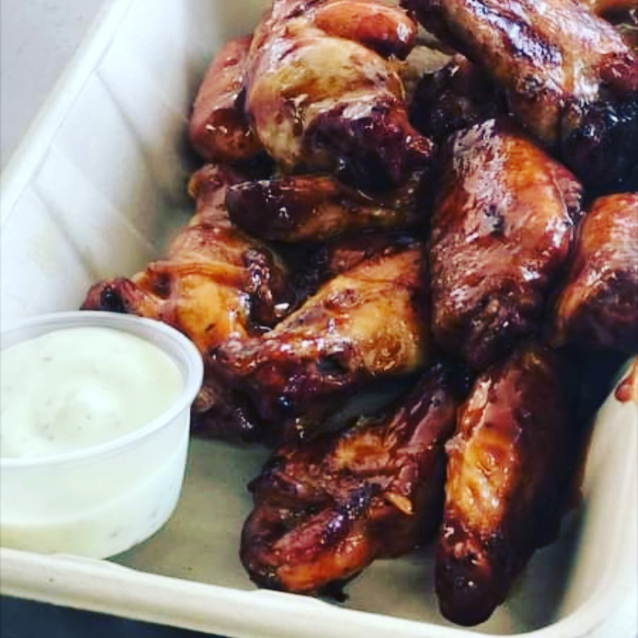 chicken wings in a disposable container with a container of sauce