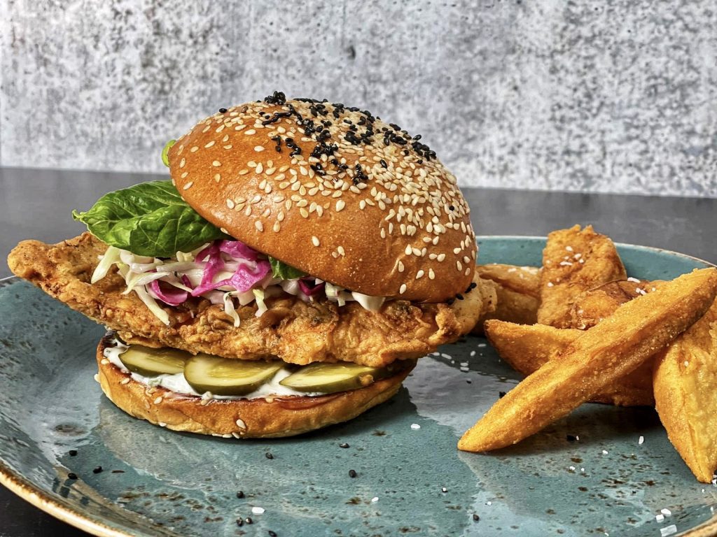a vegan chicken sandwich with thick cut fries on a blue plate