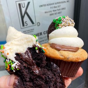 a hand holding two cupcakes in front of a kosher certificate