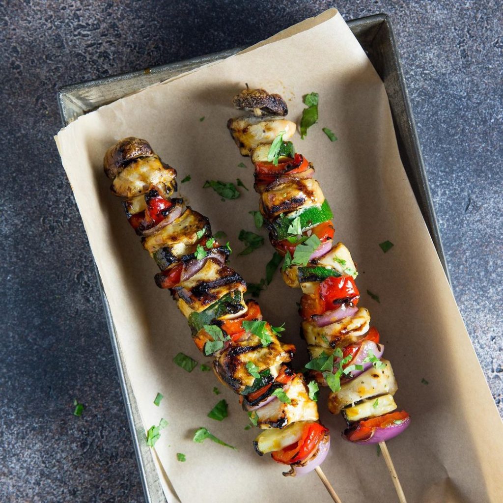 two chicken and veggie kebabs on a parchment lined tray